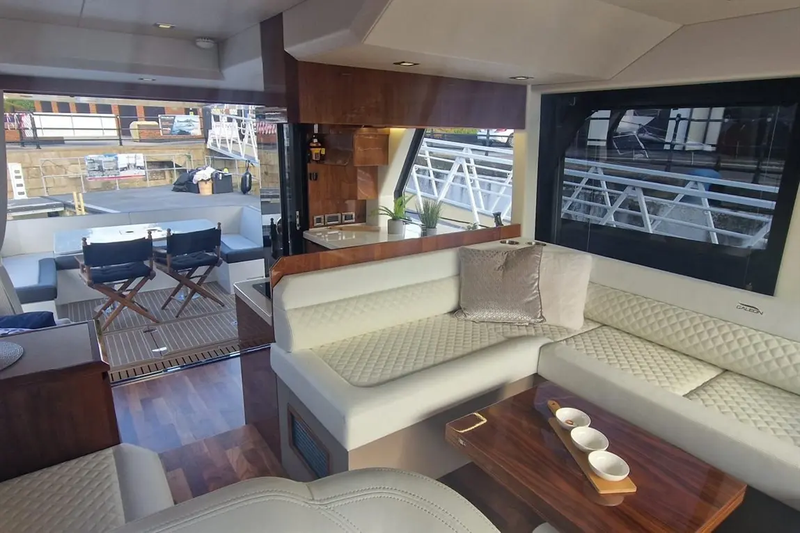 Luxury yacht interior featuring white seating, a wooden table with three bowls, and a view of the outdoor deck.